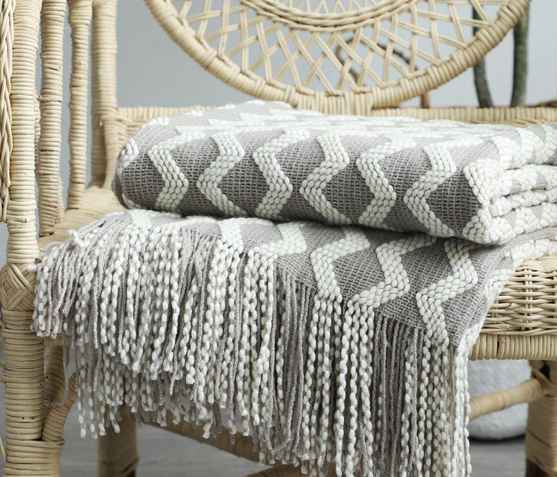 Gray and white patterned knit throw blanket with tassels on a wicker chair
