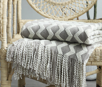 Gray and white patterned knit throw blanket with tassels on a wicker chair
