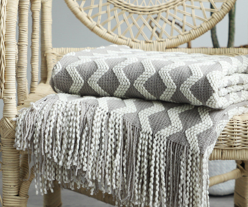 Gray and white chevron-patterned blanket with fringe draped over a wicker chair.