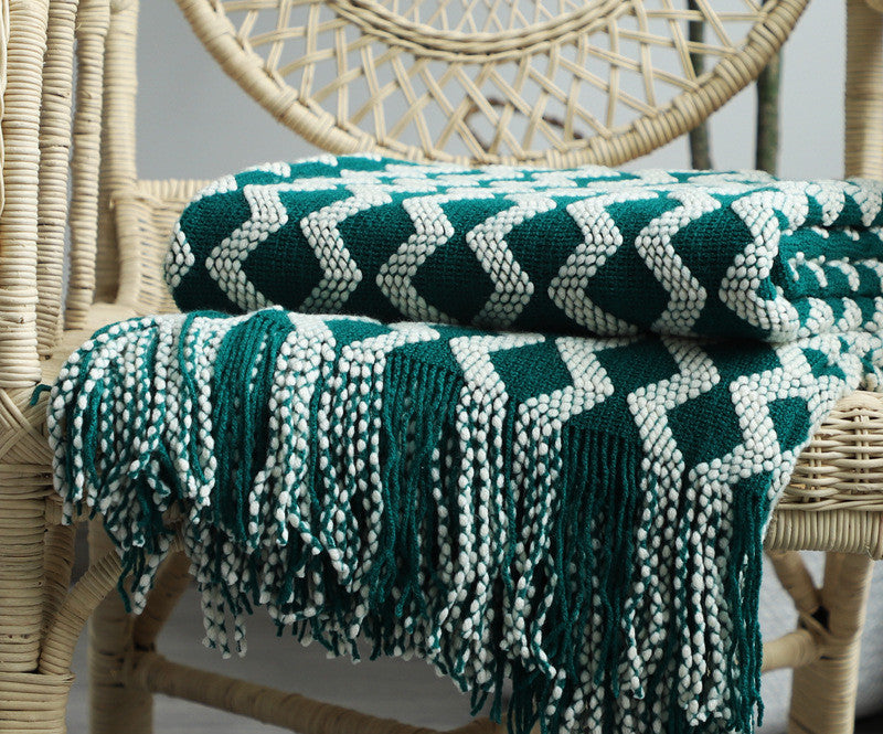 Green and white patterned knit throw blanket draped over a wicker chair.