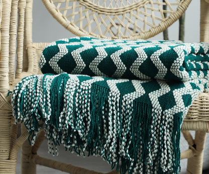 Green and white patterned knit throw blanket draped over a wicker chair.