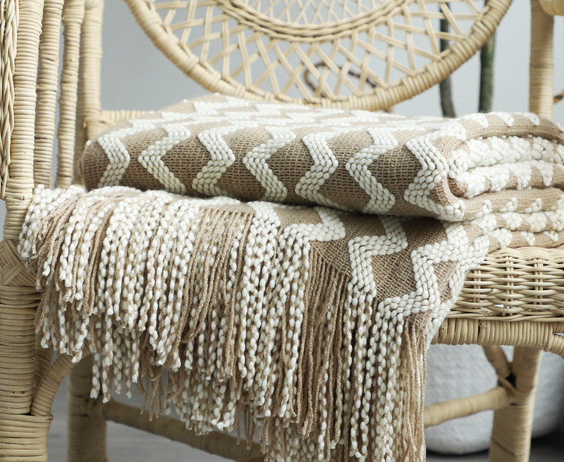 Knitted blanket with fringe draped over a wicker chair